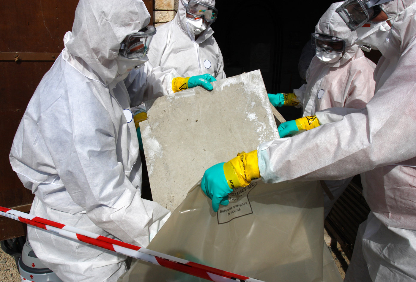 Operatives in protective suits removing asbestos sheeting